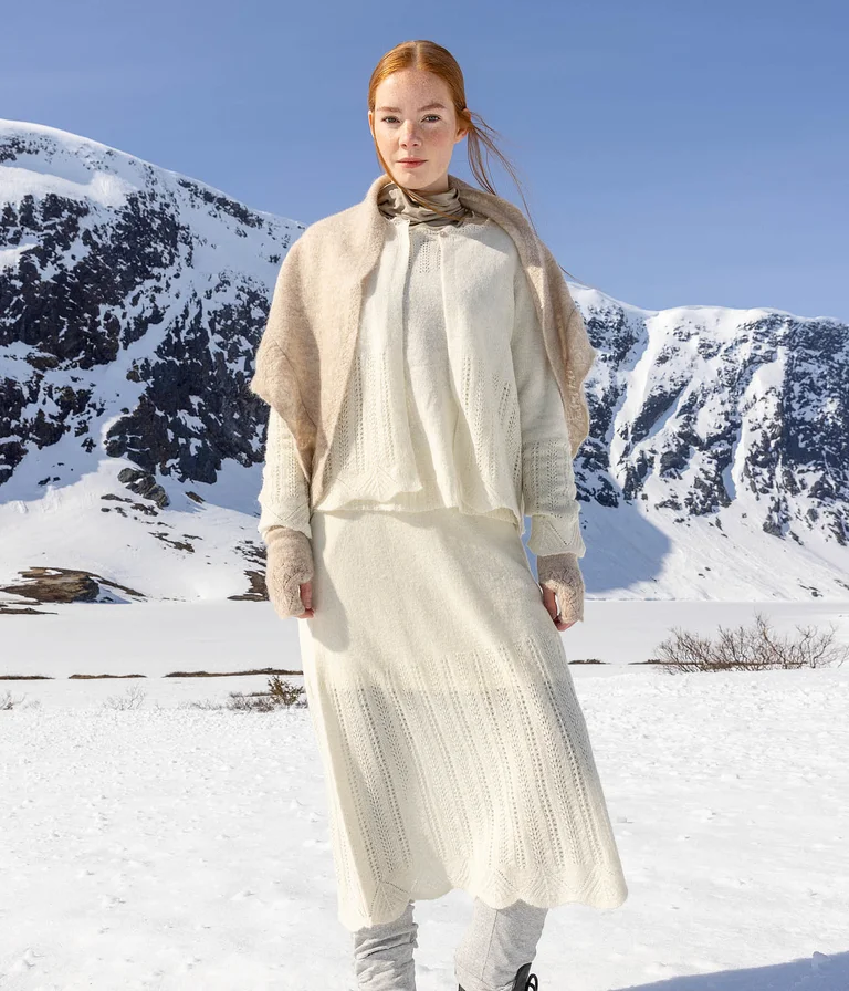 Eine Frau in verschneiter Landschaft, in weißer Strickmode aus Gudrun Sjödéns Weihnachtskollektion 2025.