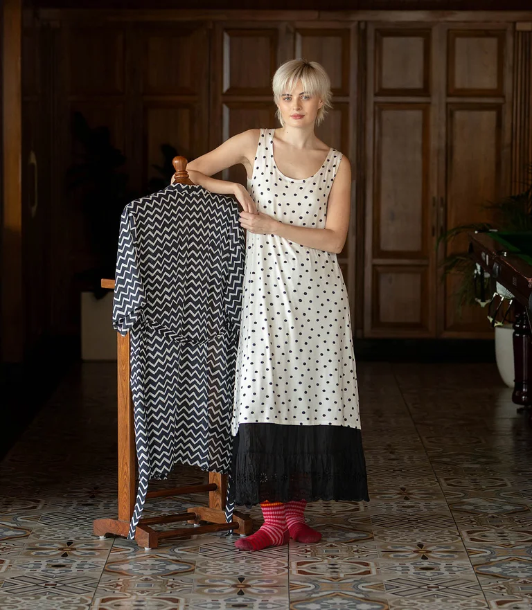 A woman wearing a white nightgown with black dots from Gudrun Sjödén.