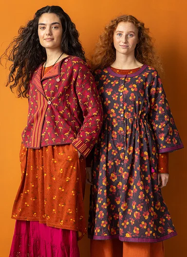 Two women wearing layers of patterned clothes in shades of red from Gudrun Sjödén. 