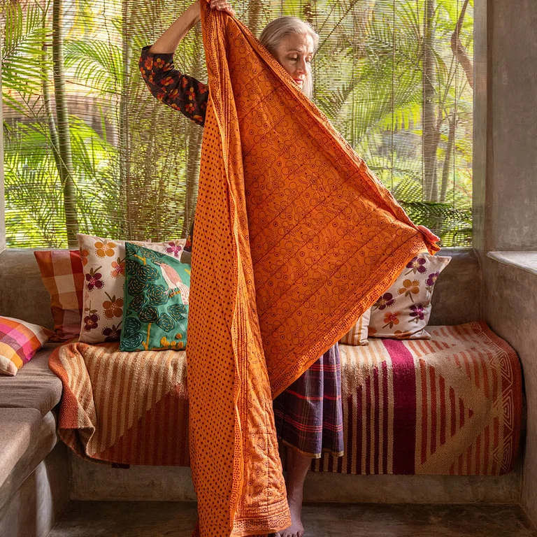 A woman standing in front of a sofa holding an orange throw from Gudrun Sjödén.