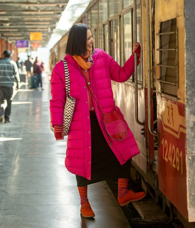 A woman wearing a long, pink down jacket from Gudrun Sjödén, about to board a train.