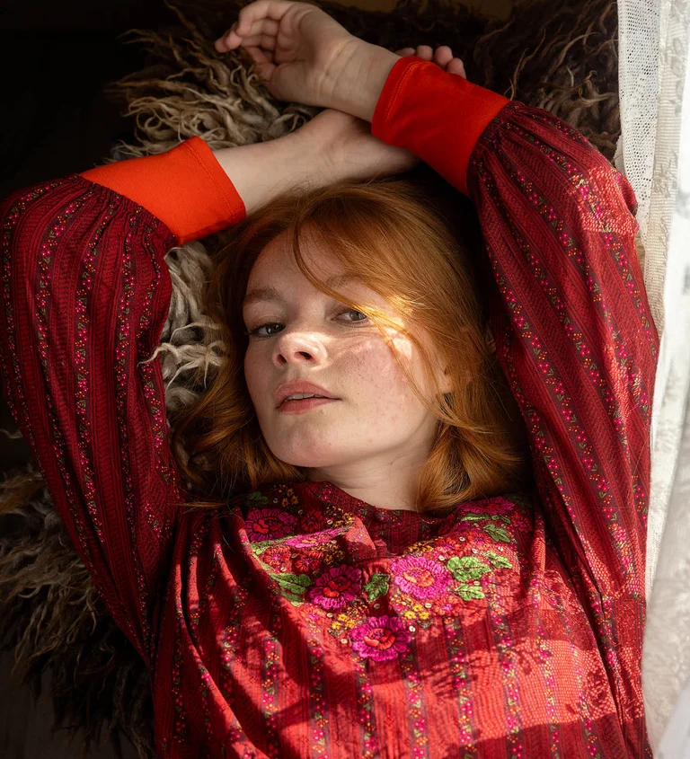 A woman lying down wearing a red, embroidered dress from Gudrun Sjödén’s 2025 Christmas collection. 