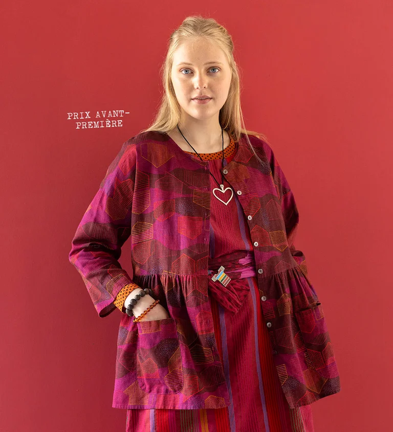 A woman wearing a red, patterned blouse and a silver heart-shaped necklace from Gudrun Sjödén’s 2025 Christmas collection. 
