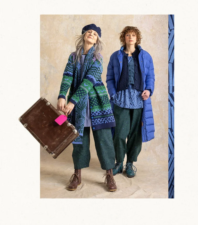 Two women wearing layers of clothing in shades of blue from Gudrun Sjödén. One of them has a suitcase in her hand.