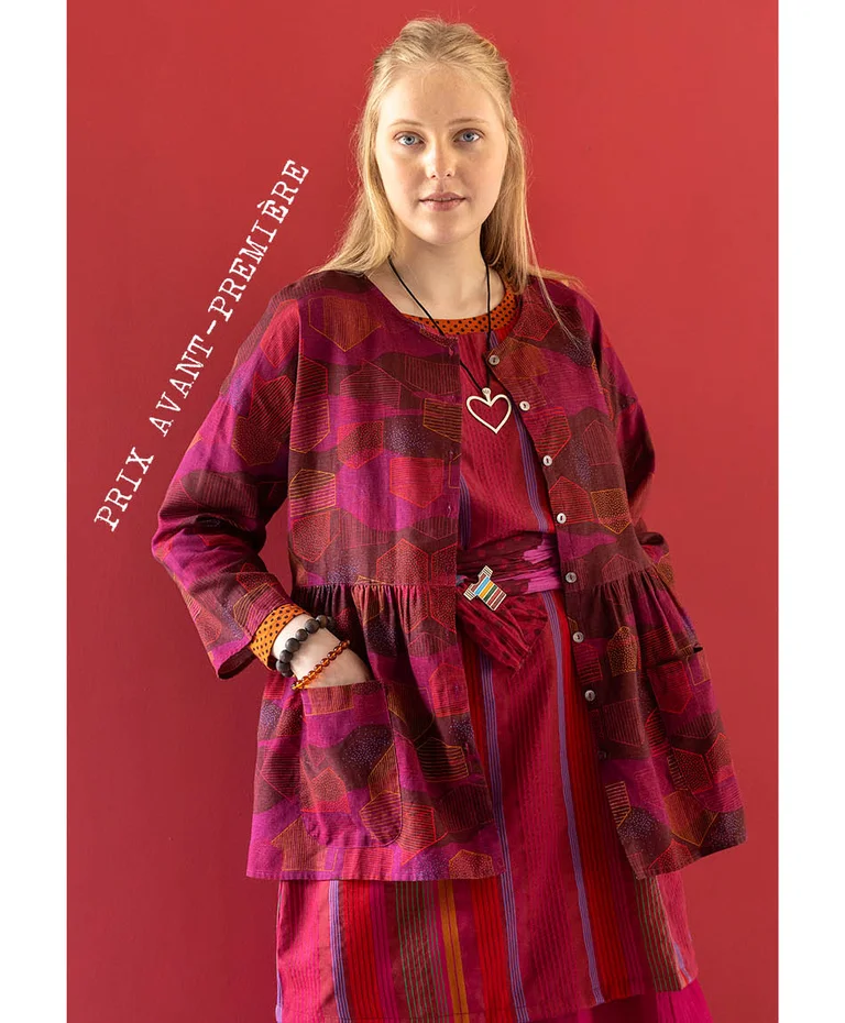 Une femme portant une blouse boutonnée rose rouge de la collection de Noël 2025 de Gudrun Sjödén. 