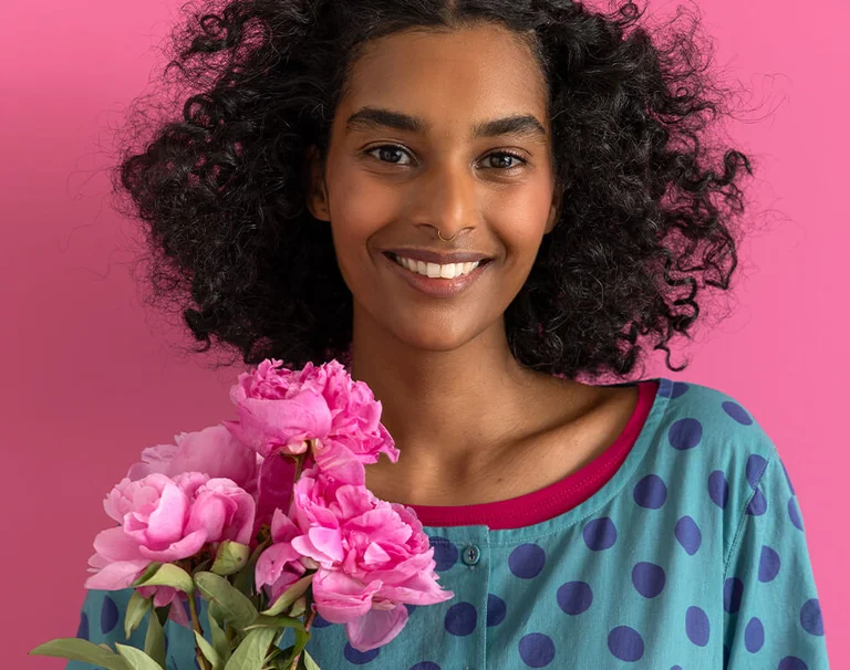 A woman holding a pink flower in her hand and wearing colourful clothes from Gudrun Sjödén.