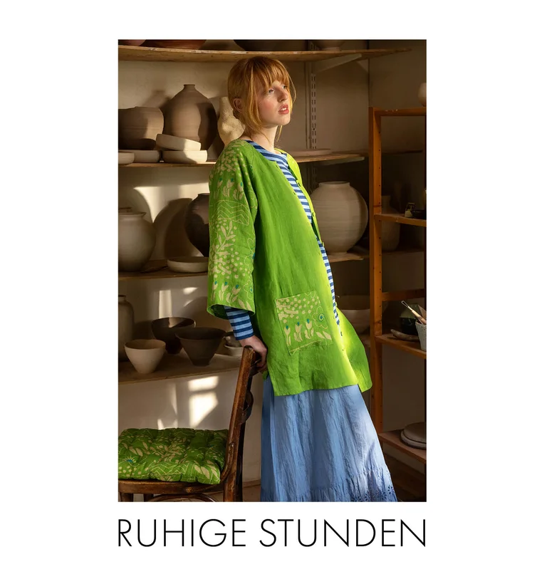 A woman in a pottery studio wearing a green “Nemorosa” linen tunic, a striped top and a light-blue skirt from Gudrun Sjödén.