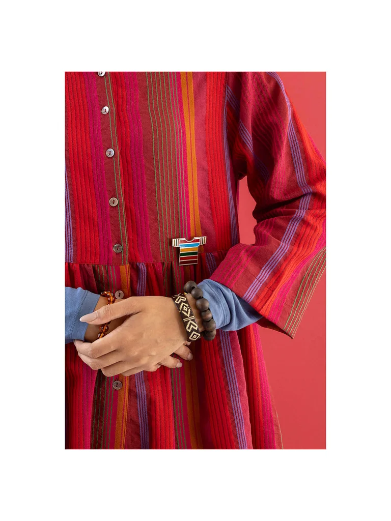 A close-up of a woman wearing a striped dress and a silver T-shirt-shape brooch from Gudrun Sjödén’s 2025 Christmas collection. 