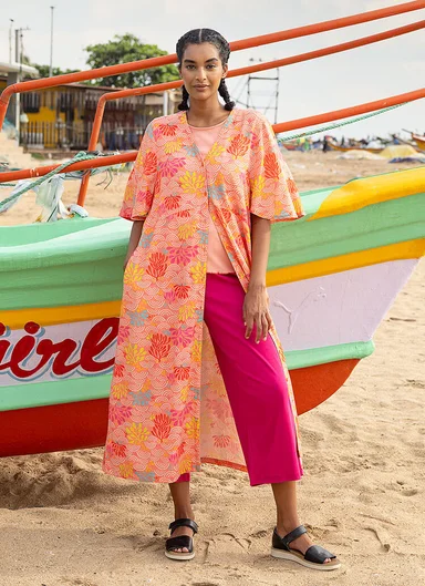 A woman standing next to a boat wearing a peach patterned dress from Gudrun Sjödén.