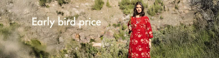 A woman holding a green branch in front of her face and wearing a red wrap dress from Gudrun Sjödén.