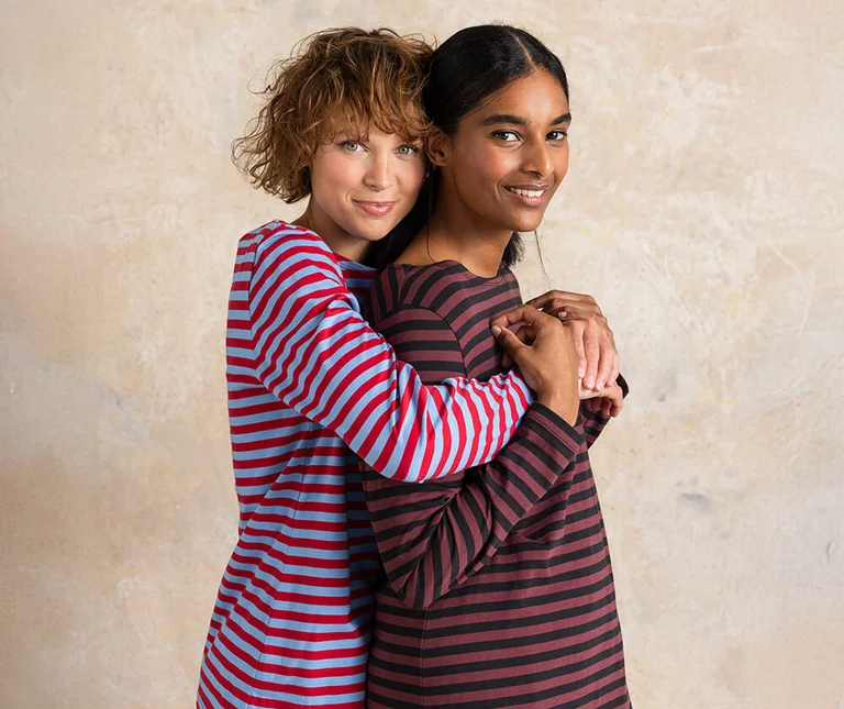 Two women embrace, wearing striped tops from Gudrun Sjödén.