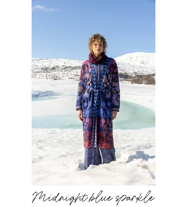 A woman standing in a snowy landscape wearing layers of clothes from Gudrun Sjödén’s 2025 Christmas collection.