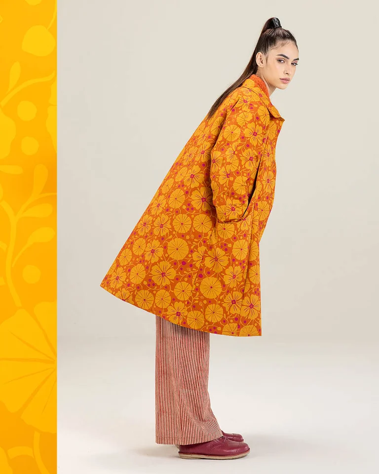 A woman photographed from the side wearing a patterned orange coat from Gudrun Sjödén.
