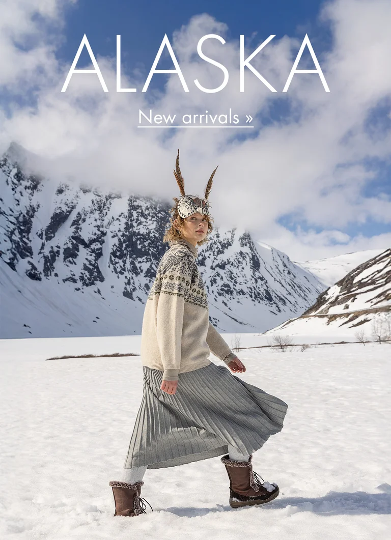 A woman walking in a snowy landscape with an animal mask on her head wearing clothes from Gudrun Sjödén’s 2025 Christmas collection.  In image: Alaska 