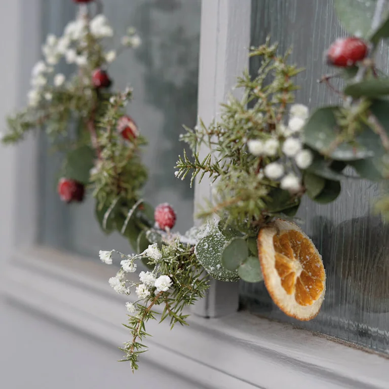 Een handgemaakte kerstkrans op een metalen ring, versierd met groen, bessen en gedroogde sinaasappel.