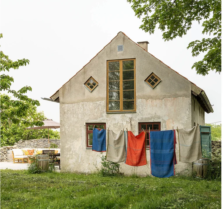 An old lime-rendered house in a verdant garden, where red, blue and natural-hued textiles from Gudrun Sjödén are hanging on a clothes line.