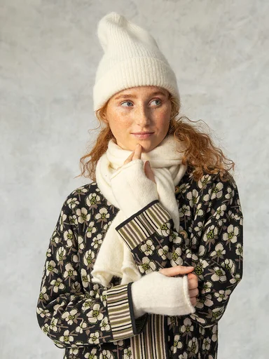 A woman wearing a white beanie, scarf and fingerless gloves from Gudrun Sjödén.