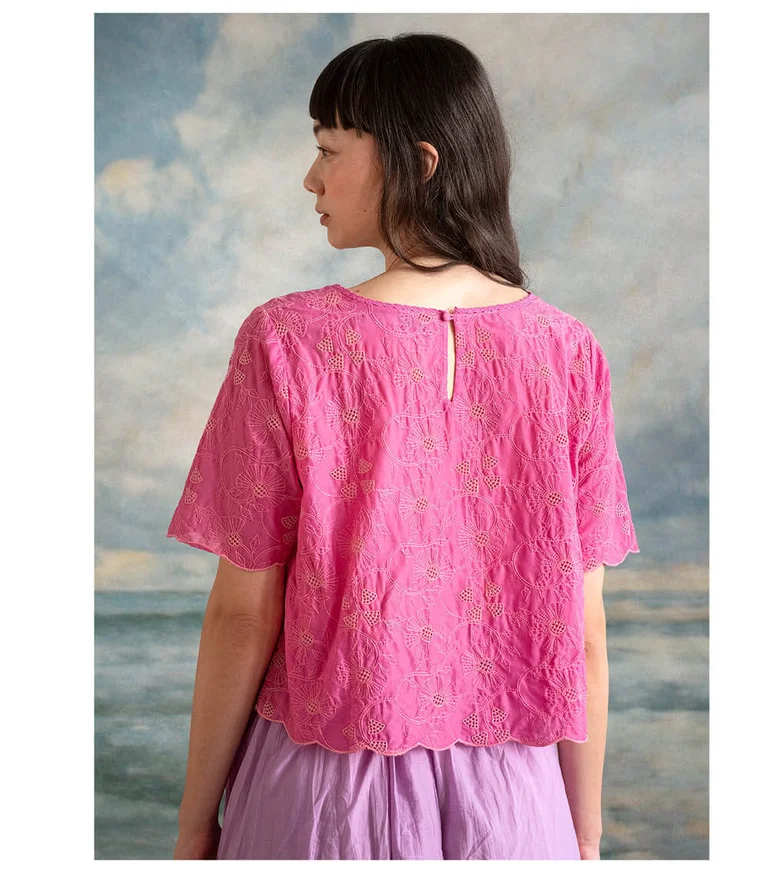 A woman facing away from the camera wearing a pink lace top and a purple skirt from Gudrun Sjödén.