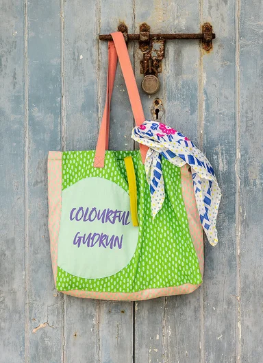 A woven bag with a shawl tied to it from Gudrun Sjödén hanging on a door handle. 