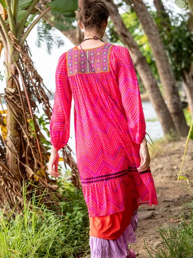 A woman facing away from the camera wearing layers of colourful clothes from Gudrun Sjödén.