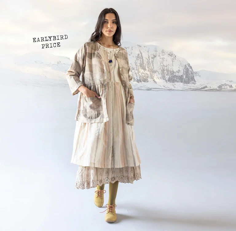 A woman standing in a snowy landscape wearing layers of white and beige clothes from Gudrun Sjödén’s 2025 Christmas collection. 