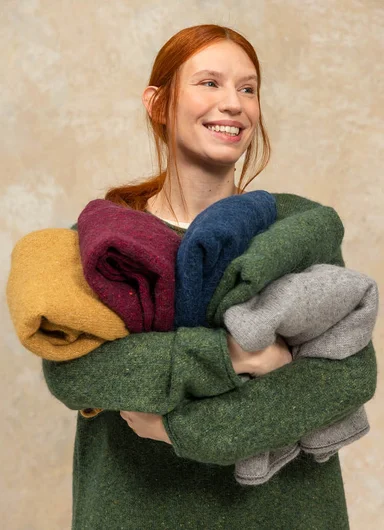 A woman with her arms full of knitwear from Gudrun Sjödén.