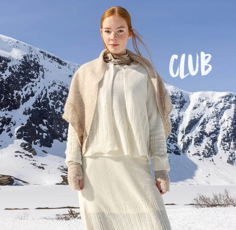 Een vrouw die in een sneeuwlandschap staat en laagjes witte en beige kleding draagt uit de kerstcollectie 2025 van Gudrun Sjödén.