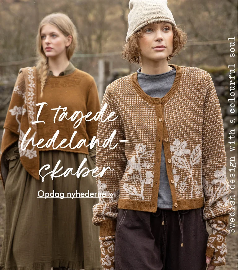 Two women standing next to each other wearing clothes in earthy hues from Gudrun Sjödén. Sheep and a stone wall are visible in the background.