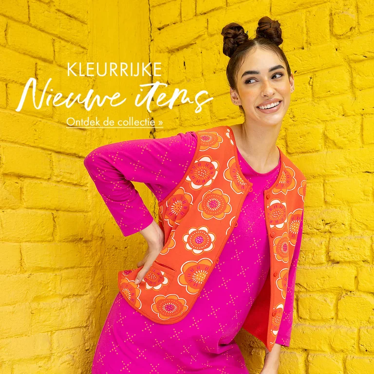 Twee vrouwen poseren tegen een gele bakstenen muur gekleed in kleurrijke kleding van Gudrun Sjödén.