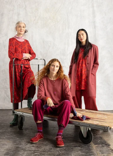 Three women wearing red and burgundy clothes from Gudrun Sjödén’s Essentials collection, photographed in a studio setting.