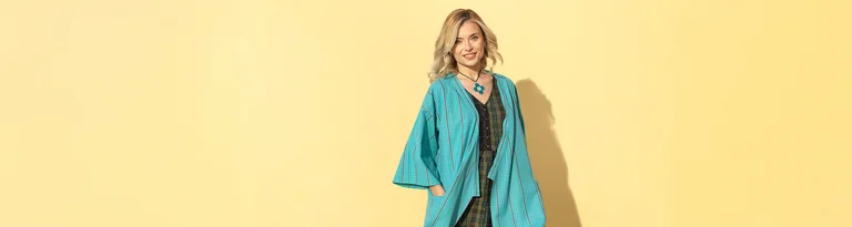 Eine Frau in einem türkisfarbenen, gemusterten Kimono und einer Blumenkette steht vor einem hellgelben Hintergrund. Neben ihr ist das Wort "CLUB" in großen, türkisfarbenen Buchstaben geschrieben.