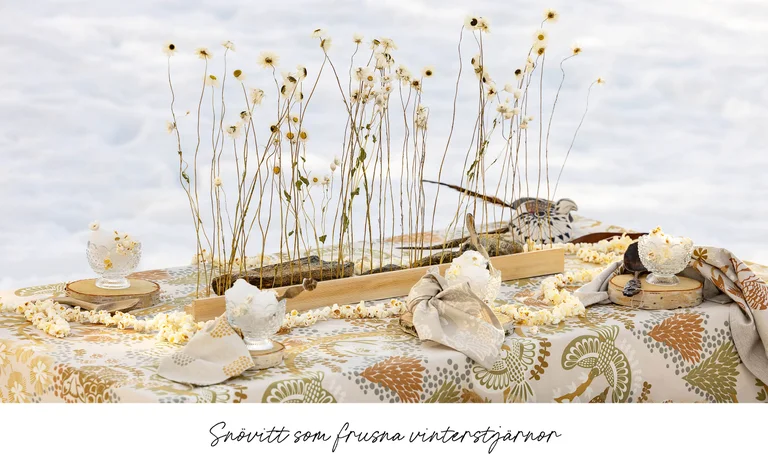 A table in the snow laid with home textiles from Gudrun Sjödén’s 2025 Christmas Home collection.