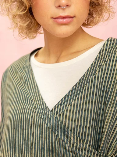 A close-up of the upper body of a woman wearing a striped woven garment from Gudrun Sjödén.