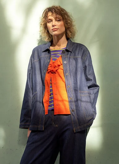 A woman wearing a denim jacket over an orange ruffle blouse from Gudrun Sjödén.