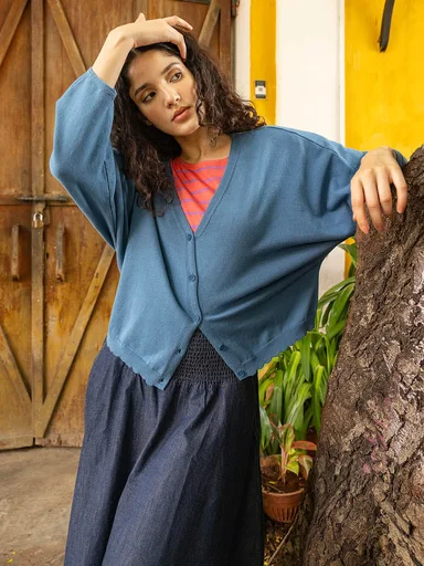 A woman wearing a denim jacket over an orange ruffle blouse from Gudrun Sjödén.