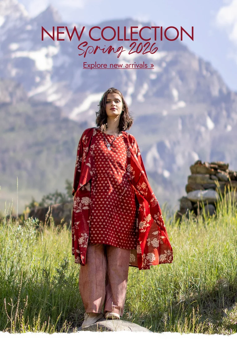 A woman standing in a mountain landscape wearing layers of red, woven clothes from Gudrun Sjödén.