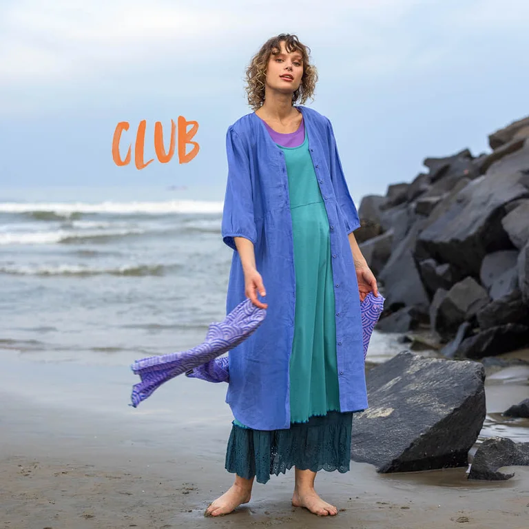 A woman standing on a beach wearing layers of clothes from Gudrun Sjödén.