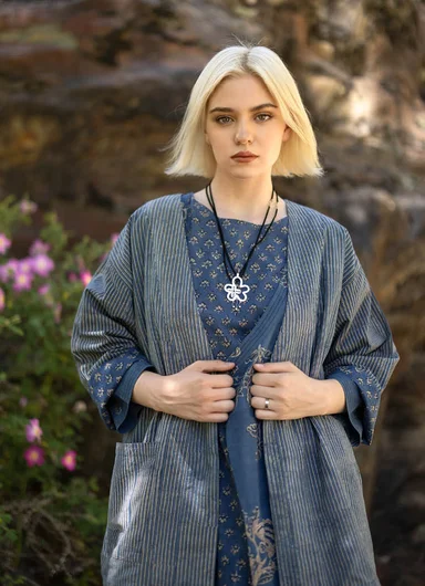 A close-up of the upper body of a woman wearing a striped woven garment from Gudrun Sjödén.