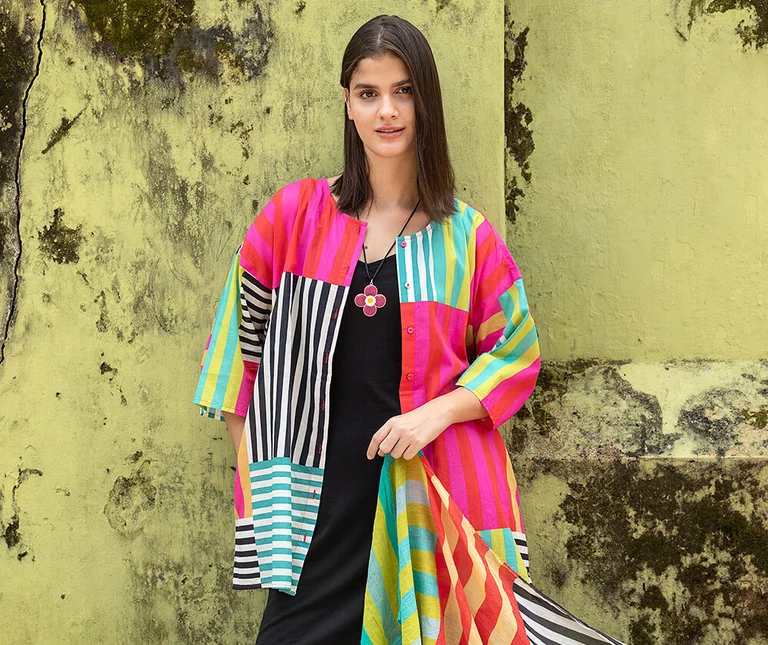 A woman wearing a colourful striped blouse from Gudrun Sjödén. Holding a matching scarf in her hand.