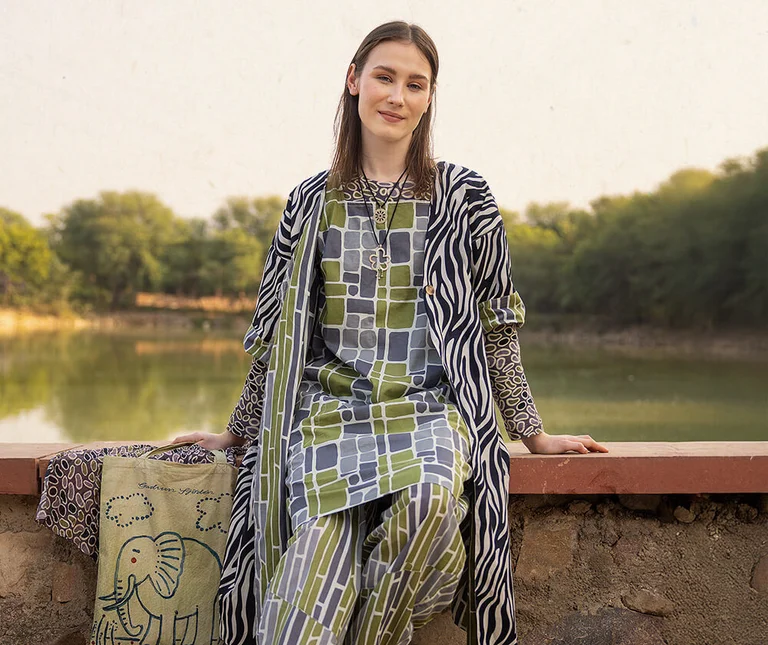A woman sitting on a wall wearing patterned organic cotton clothes from Gudrun Sjödén.
