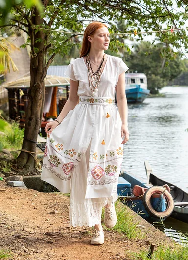 A woman holding a large, green leaf wearing layers of orange clothes from Gudrun Sjödén.