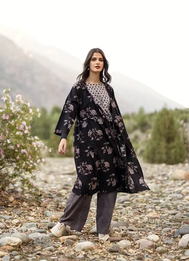 A woman standing in the countryside wearing layers of black and grey clothes from Gudrun Sjödén.