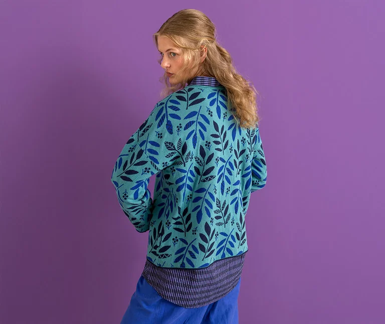 A woman with her back half-turned to the camera wearing a turquoise, patterned cardigan from Gudrun Sjödén.