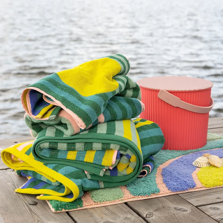 Colourful terry towels and a bath mat from Gudrun Sjödén on a jetty by the water.
