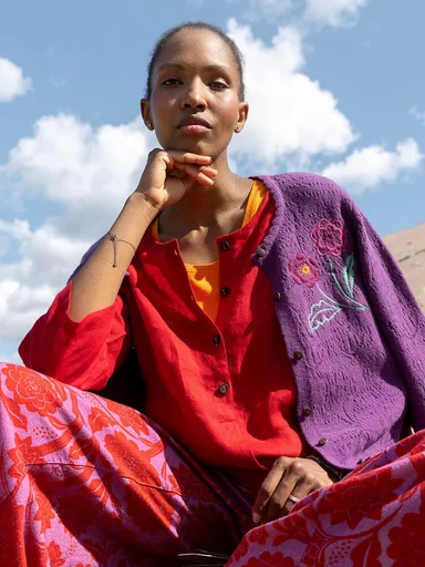 A woman sitting down wearing colourful clothes from Gudrun Sjödén.